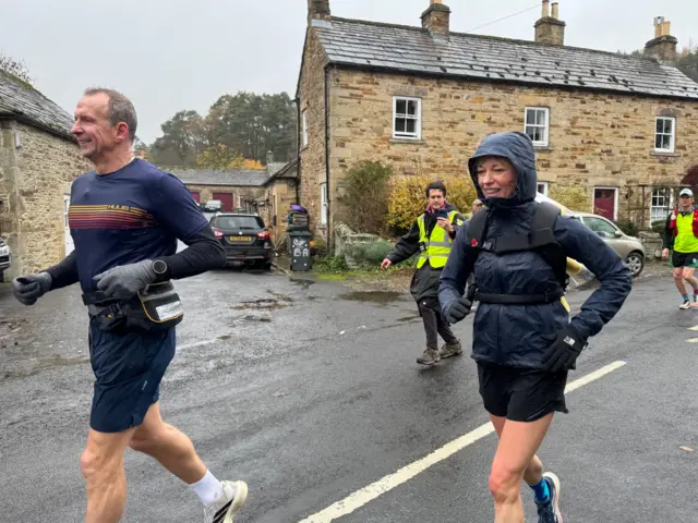 Sara Cox running in a rain coat