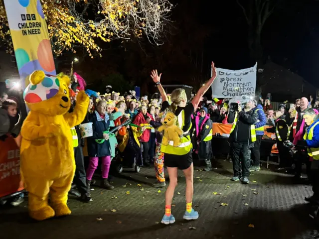Sarah raises her arms in celebration towards the crowd after crossing the finish line
