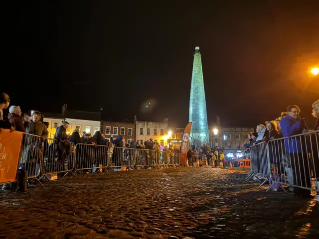 A crowd of people behind barriers on a cobbled street