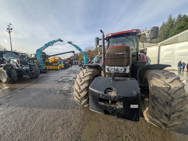 A line of tractors in a muddy field, with a red tractor at the front