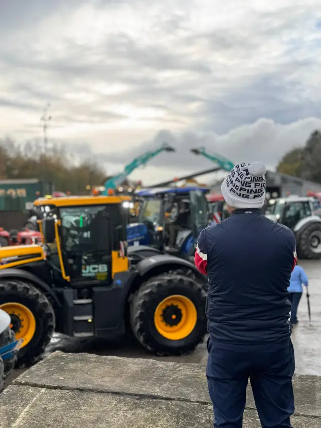 A man faces away looking at a gathering of tractors.