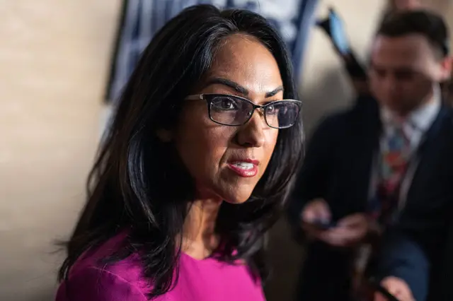 Lauren Boebert speaks at Capital Hill. She is wearing a purple dress and eye glasses.