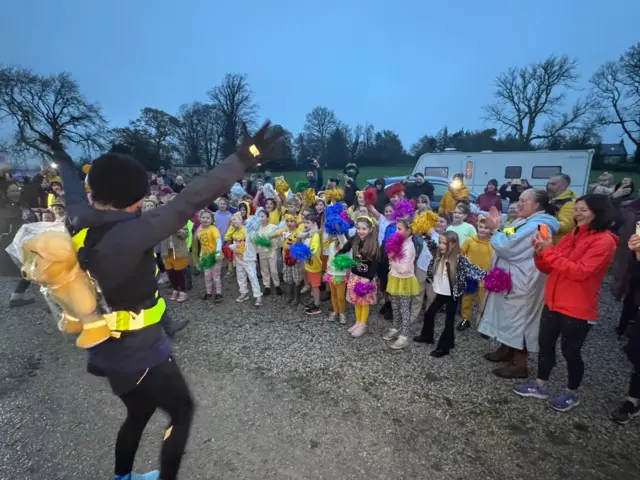 Sara raises her arms in front of a group of schoolkids