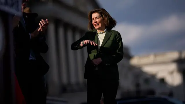 Nancy Pelosi stands on the steps of the Capitol wearing a green suit