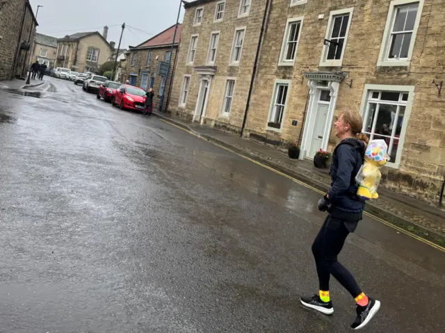 Sara Cox running in the rain, with Pudsey in a raincoat on her back