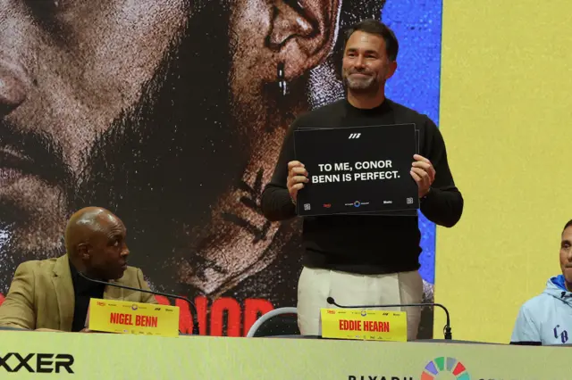 Eddie Hearn holds up a placard that says 'To me, Conor Benn is perfect'