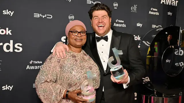 Bus Aunti and Morgan M-James smile at the camera as they hold up they TikTok awards