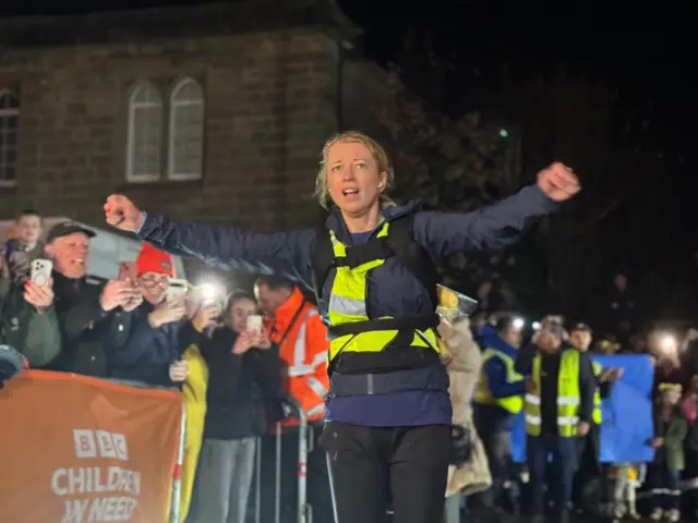 Sara raises her arms in front of a crowd at the finish line
