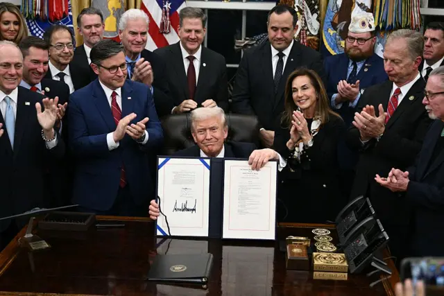 Trump holds up the bill he signed, as he is cheered by Republicans around him