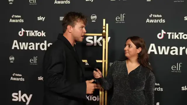 Yasmin interviews Max who stands with a ladder