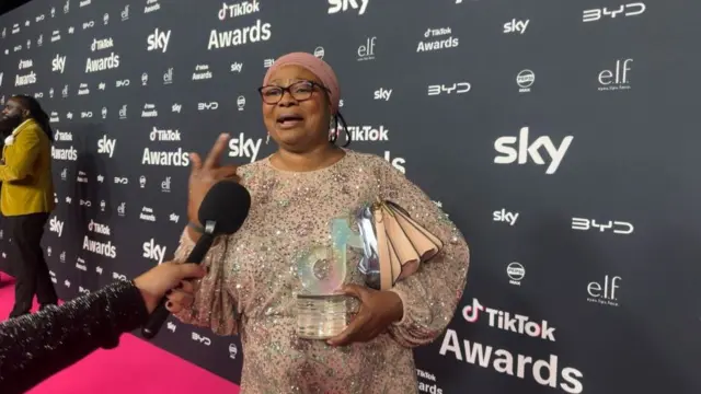 Bus Aunty holding her award on the TikTok awards red caroet