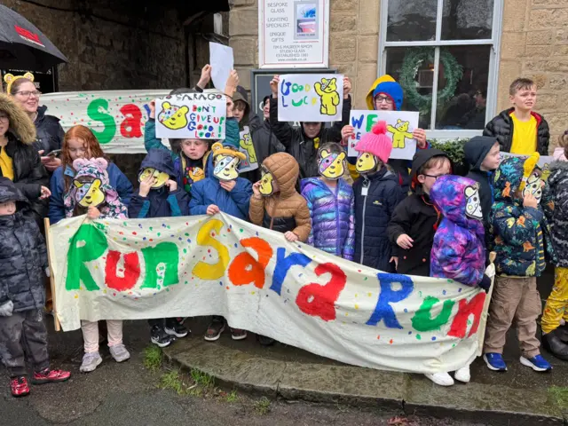 Kids hold a banner saying 'Run Sara, Run!'
