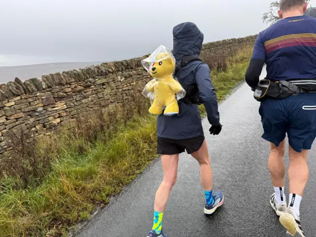 Sara runs with her Pudsey backpack dressed in a raincoat
