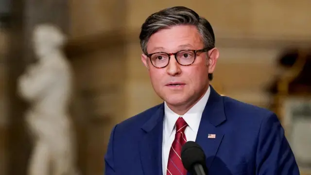 US House Speaker Mike Johnson wears a navy suit and red tie as he speaks during a media conference