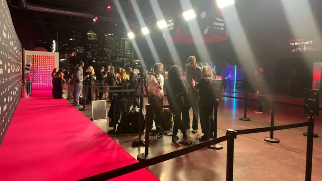 A group of journalists huddle around the red carpet.