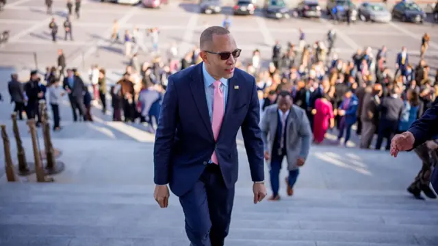 Hakeem Jeffries walks up the steps of the Capitol in a navy suit and pink tie