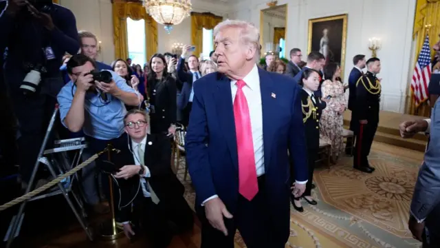 President Donald Trump in a bright red tie and blue suit walking out of a crowded room