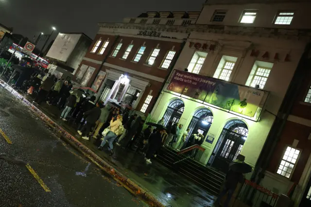 People wait outside in the rain to enter a building