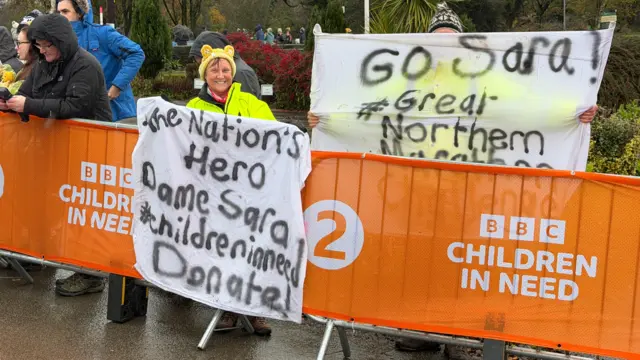 A woman holding a banner to cheer on Sara Cox, it reads Hero Dame Sara Children in Need donate