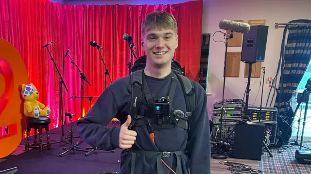 A man wearing a blue jumper and a black vest with a camera on it