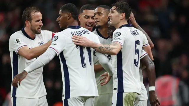 Harry Kane, Marcus Rashford, Morgan Rogers, Ezri Konsa, Bukayo Saka and John Stones celebrate together after Saka's goal.