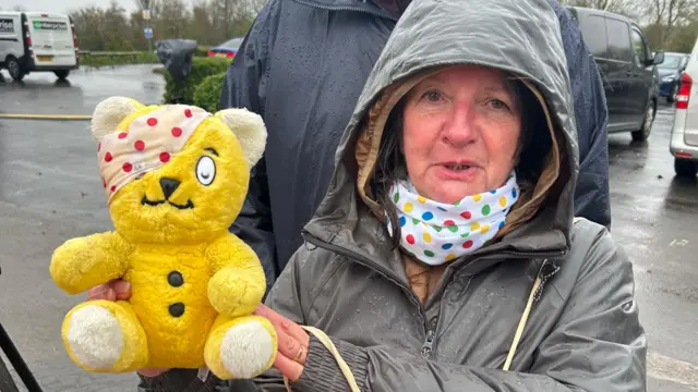 A woman holding a Pudsey bear in a rain coat