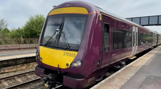 A purple train with a yellow front at a platform