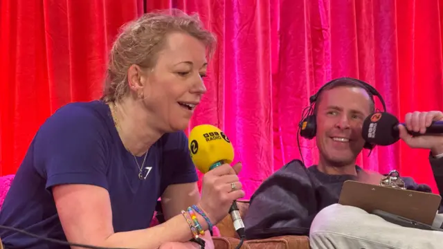 Sara Cox in front of a red curtain holding a microphone