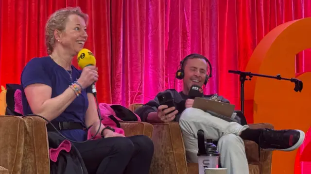 Sara and Scott sit on chairs with a red curtain behind them