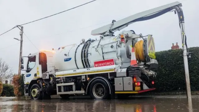 A white lorry with a long tube at the back parked in a pool of water