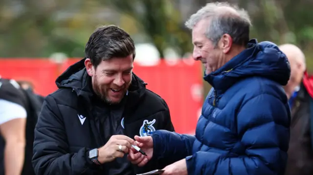Bristol Rovers manager Darrell Clarke signs an autograph for a fan at Accrington
