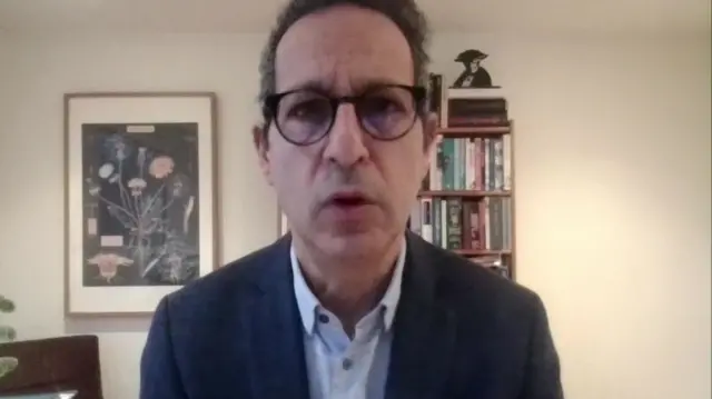 Enver Solomon in a blue shirt and blue jacket sits in a cream living room