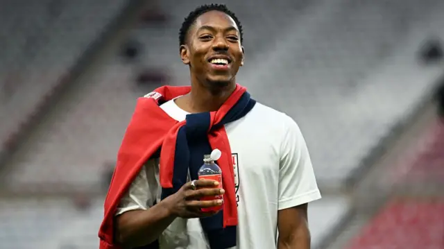 Myles Lewis-Skelly smiles for the camera while holding up a bottle of water.