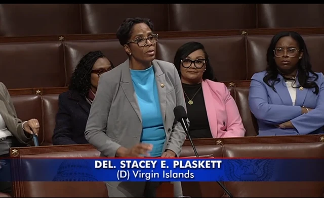 Plaskett wearing a grey jacket over a turquoise shirt speak on the floor of the House of Representatives