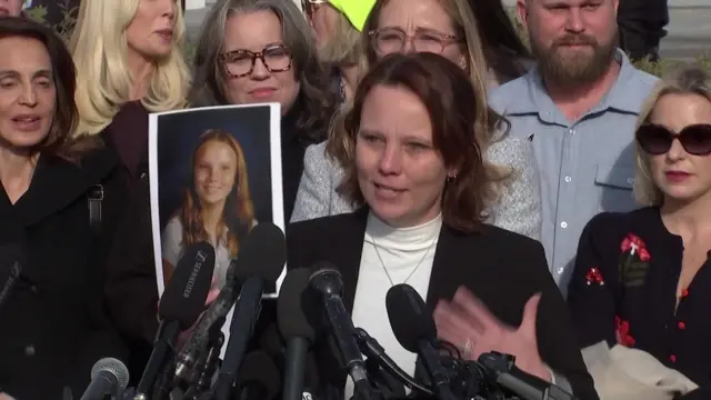 Survivor Jena-Lisa Jones holds a photo of her as a 14-year-old girl as she speaks at a media conference while supporters stand behind her