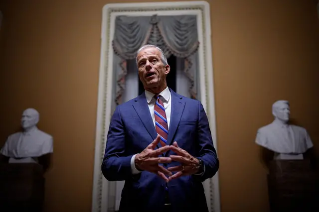 Senate Majority Leader John Thune stands between two busts of historical US political figures