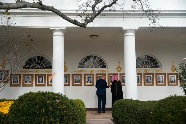 The backs of Trump and MBS, as they look at a gallery of photos of US presidents