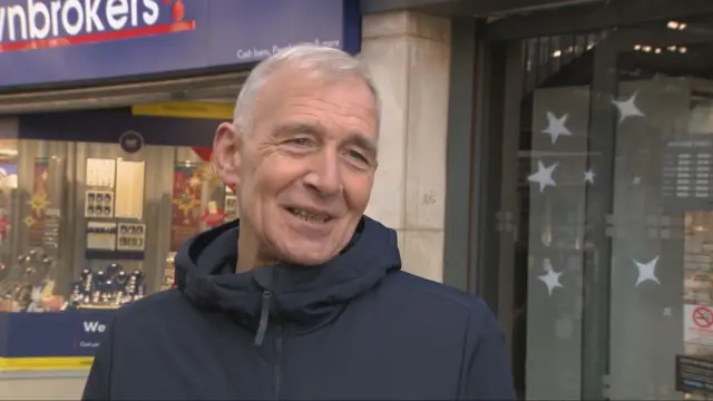 Billy smiles, he has white hair and wears a blue jacket.