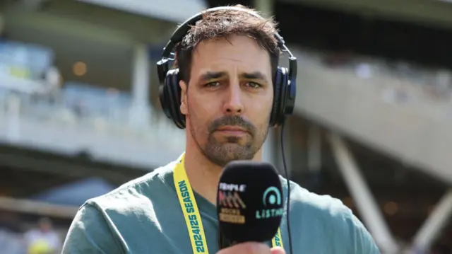 Mitchell Johnson wearing headphones and holding a microphone up to his mouth.