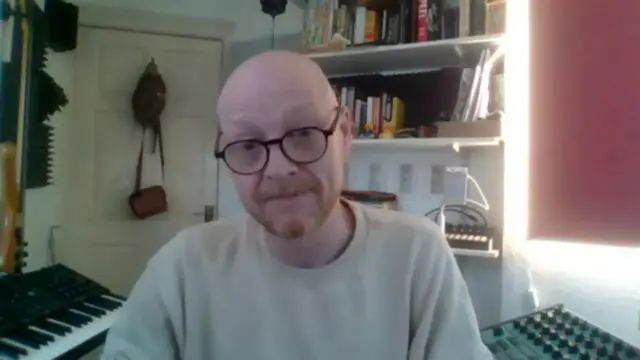 Boyd Sleator, a man with a shaved head, a ginger beard and dark-rimmed glasses, looks at the camera during a video call interview. He is wearing a cream or pale crew-necked sweat shirt.