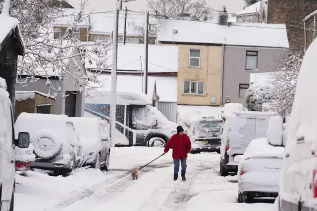Person walks dog along snow-filled road in County Durham