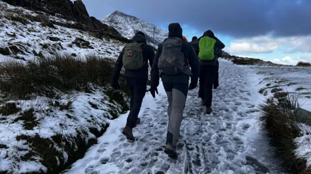 People wearing cold-weather clothing walk along a path, which is covered in snow
