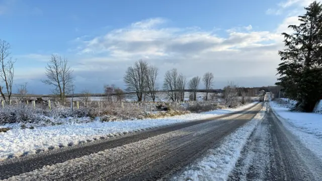 A road covered in snow, with tracks where vehicles have travelled along, creating mushy ice