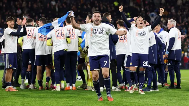 John McGinn celebrates while waving a Scotland flag with his team-mates in the background.