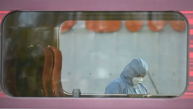 A forensics official is seen through the window of a stationary train.