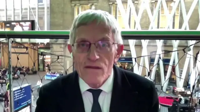 Simon Calder sitting down  near the balcony banister of King's Cross station