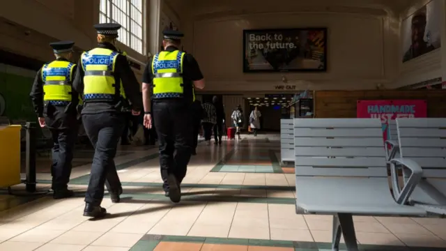 Three British Transport Police walk across the main hall of a train station in the UK