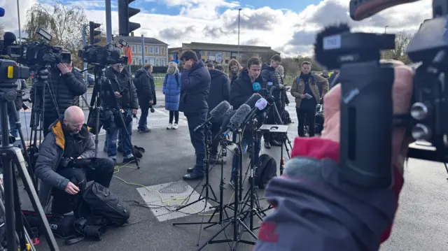 Journalists gathered on a street with cameras and equipment around them.