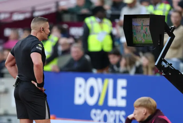 Referee Rob Jones checks his pitchside monitor