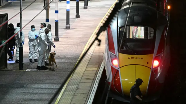Police officers and a dog handler work on the platform alongside an LNER Azuma train at Huntingdon Station in Huntingdon.